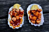 two portions of curry sausage on paper plates on a dark wooden table