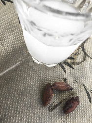a glass of ouzo and three seeds of olives on a paper tablecloth with olive design