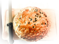 a freshly baked light brown raisin bread on a wooden board to that a knife to cut the first slice