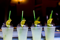 four cold softdrinks in plastic cups with drinking straws and lemon slices