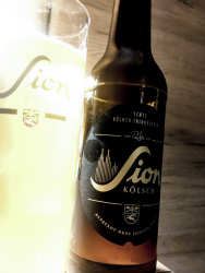 the german beer sion kölsch in a bottle and in a shining glass in front of a wooden wall