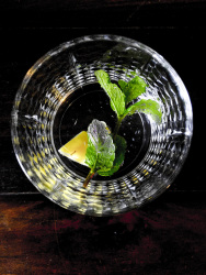 a glass of water with peppermint leaves and a peace of ingwer on a dark wooden table