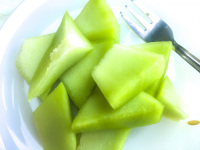 some peaces of honeydew melon are laying on a white plate with a fork ready to eat it