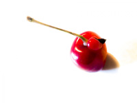an unique cherry is laying on a white wooden table and casts a small shadow
