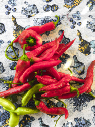 red pepperoni and some green ones are laying on a colorful tablecloth