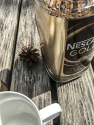 a pine cone, a big glass of nescafe and en empty white cup are waiting for a nice outdoor coffee time