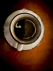 on a light brown wooden table is standing a white cup with very black coffee