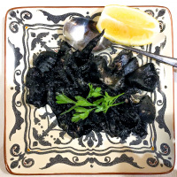 a meal with black squid to that a spoon, a half lemon and parsley