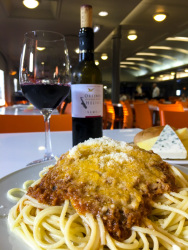 a plate spaghetti bolognese, a plate of various cheese and a bottle and a glass of greek red wine