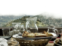 carafes, glasses, a basket and bread in front of a foggy mountain landscape