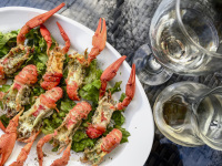 a plate boiled crayfishes and green salad next to a carafe and a glass of white wine