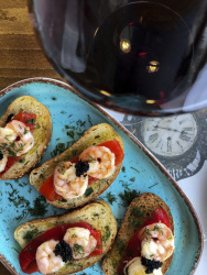 a glass red wine next to some canapes with red fried peppers, shrimps, caviar and dill