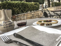 a plate with knifes and forkes and serviettes, a plate of olives and taralli and a ceramic carafe red wine