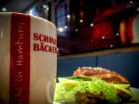 a big mug coffee next to a sandwich with cheese and green salad