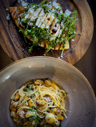 a plate of spaghetti with seafood and a dark wooden board filled with ciabatta with arugula and parmesan