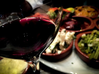 a glass red wine in front of some light brown ceramic bowls filled with tapas