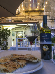 some peaces of pizza bread and a primitivo di manduria in front of an illuminated trattoria