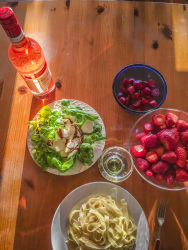 a little meal on a sunny table with tagliatelle, salad, tomatoes, strawberries and rose wine