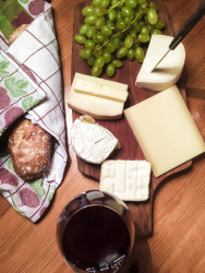 picknick with a wooden board with various cheese, bread in a towel and red wine in a glass