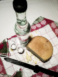 picknick on a towel with a cheese wheel, a knife, two glasses and a bottle of the greek booze named souma