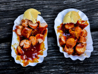 two portions of curry sausage on paper plates on a dark wooden table