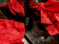 after an eaten up meal there are red crunched up serviettes on a dark brown wooden table