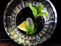 a glass of water with peppermint leaves and a peace of ingwer on a dark wooden table