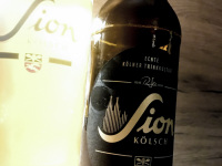 the german beer sion kölsch in a bottle and in a shining glass in front of a wooden wall