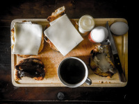 a wooden breakfast board is filled with a cup of black coffee, eggs, salt and bread rolls with marmalade and cheese