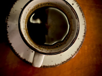 on a light brown wooden table is standing a white cup with very black coffee