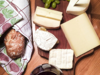 picknick with a wooden board with various cheese, bread in a towel and red wine in a glass