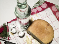 picknick on a towel with a cheese wheel, a knife, two glasses and a bottle of the greek booze named souma