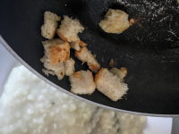 peaces of white bread are fried with oil in a pan to top the greek trachana