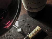 a glass of red wine, a cork and a bottle of wine from puglia on a dark wooden table