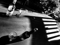 on an old wooden table you see shadow and two bottles of wine with two glasses for it, black-and-white
