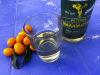 some kumquats with a bottle retsina and a glass of it on a blue table