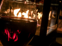 a fire lantern is reflecting in a glass of red wine