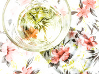 on a tablecloth with light pink flowers is standing a glass of white wine