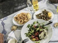 a typical big greek meal with greek salad, calamares, small fishes, garlic sauce and a bottle cair retsina