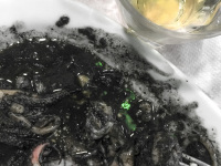 a portion black squid on a plate next to a glass of retsina