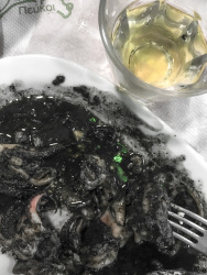 a portion black squid on a plate next to a glass of retsina