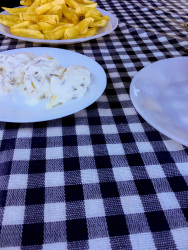 three white plates with potatoes and tzatziki on a blue white checkered tablecloth