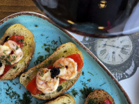 a glass red wine next to some canapes with red fried peppers, shrimps, caviar and dill