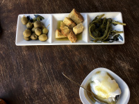 one little bowl with yogurt with honey and one of olives, bread and vegetables on a dark wooden table
