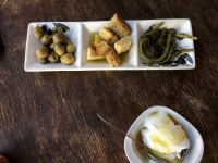 one little bowl with yogurt with honey and one of olives, bread and vegetables on a dark wooden table
