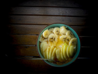on a dark wooden table is standing a turquoise bowl with peaces of bananas and apples with cinnamon and honey