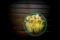 on a dark wooden table is standing a turquoise bowl with peaces of bananas and apples with cinnamon and honey