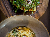 a plate of spaghetti with seafood and a dark wooden board filled with ciabatta with arugula and parmesan