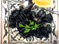 a meal with black squid to that a spoon, a half lemon and parsley
