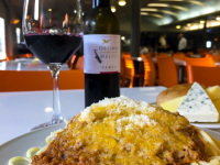 a plate spaghetti bolognese, a plate of various cheese and a bottle and a glass of greek red wine